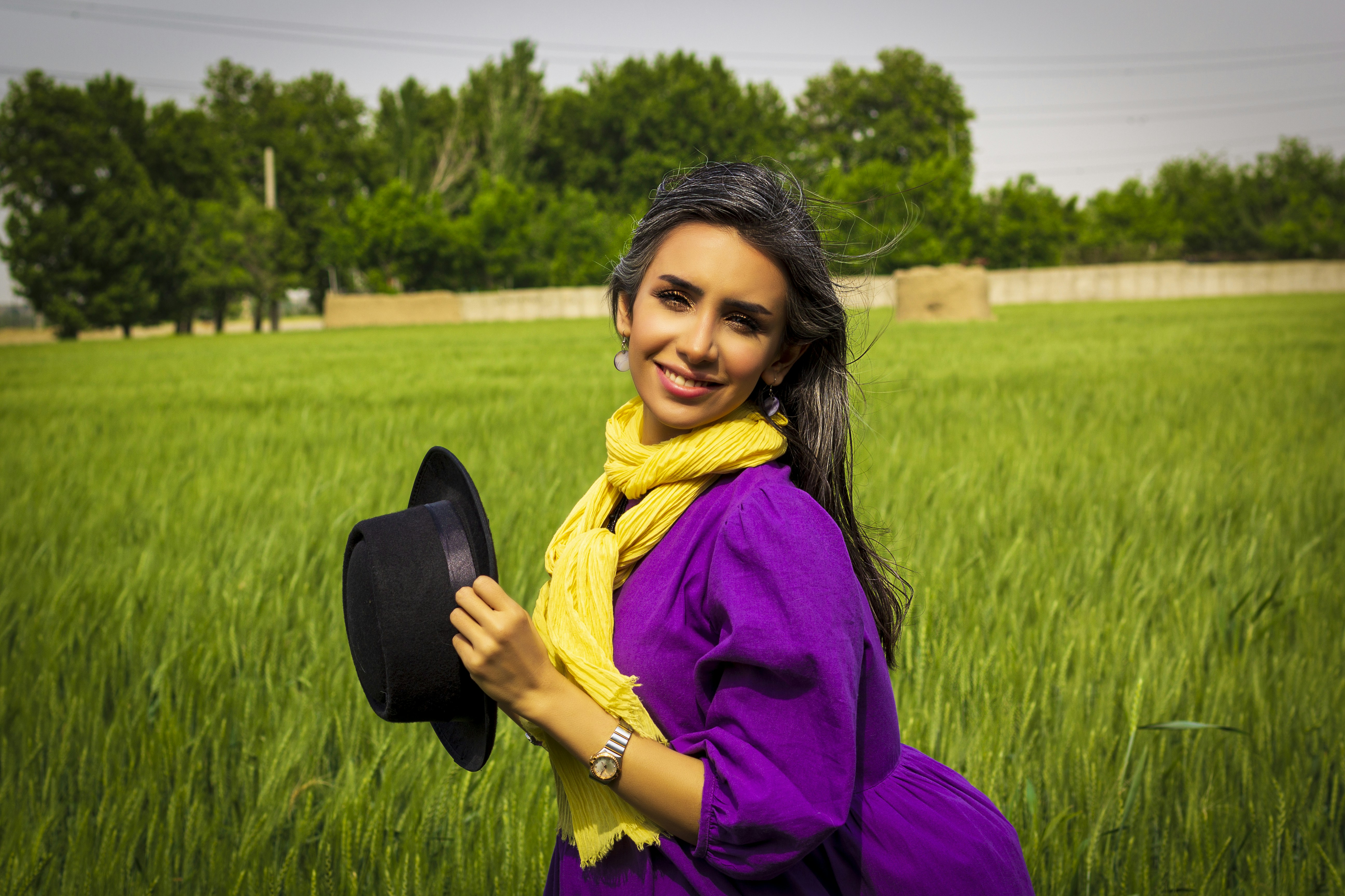 woman in purple long sleeve shirt and yellow scarf standing on green grass field during daytime