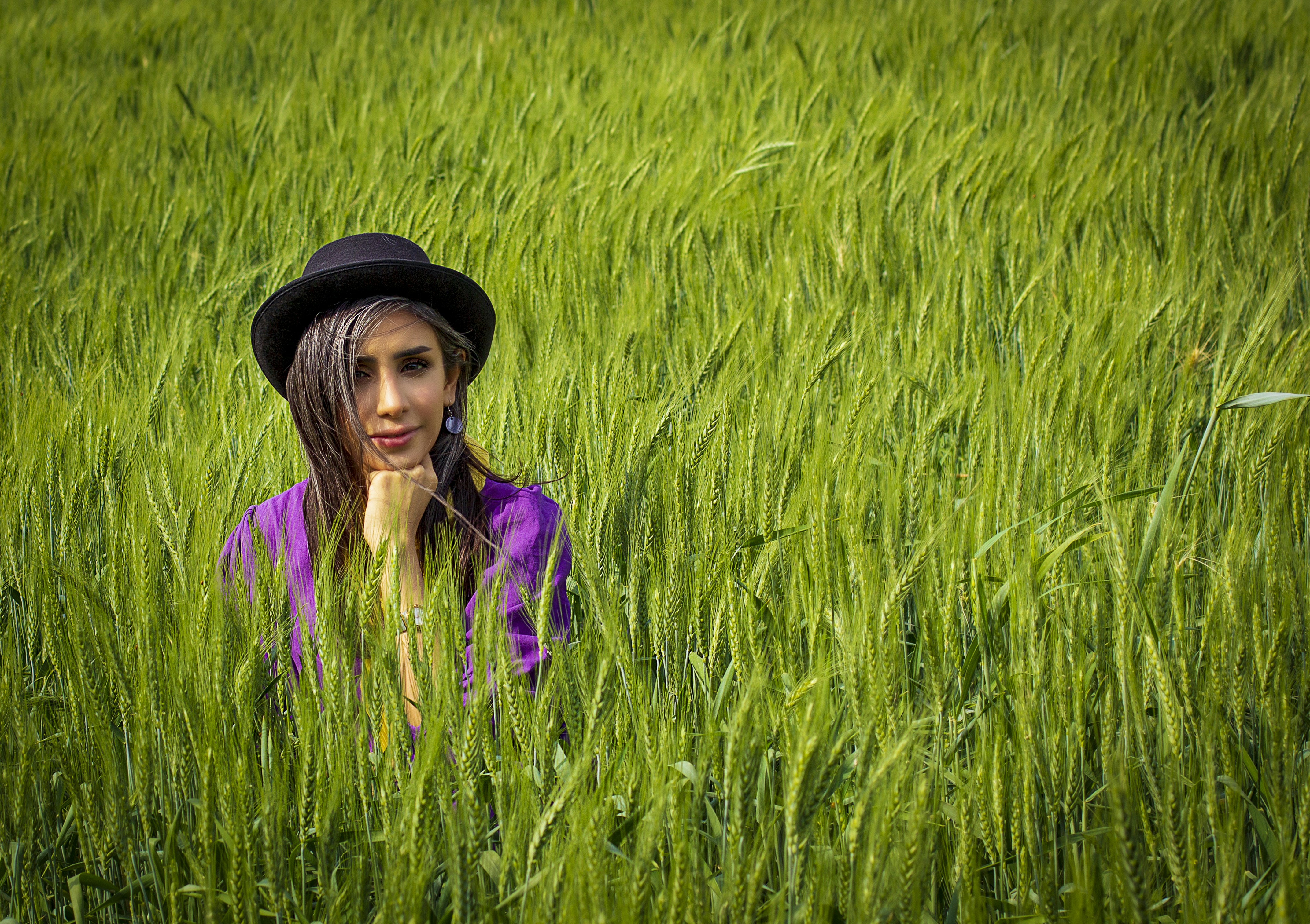 woman in purple shirt wearing black hat standing on green grass field during daytime