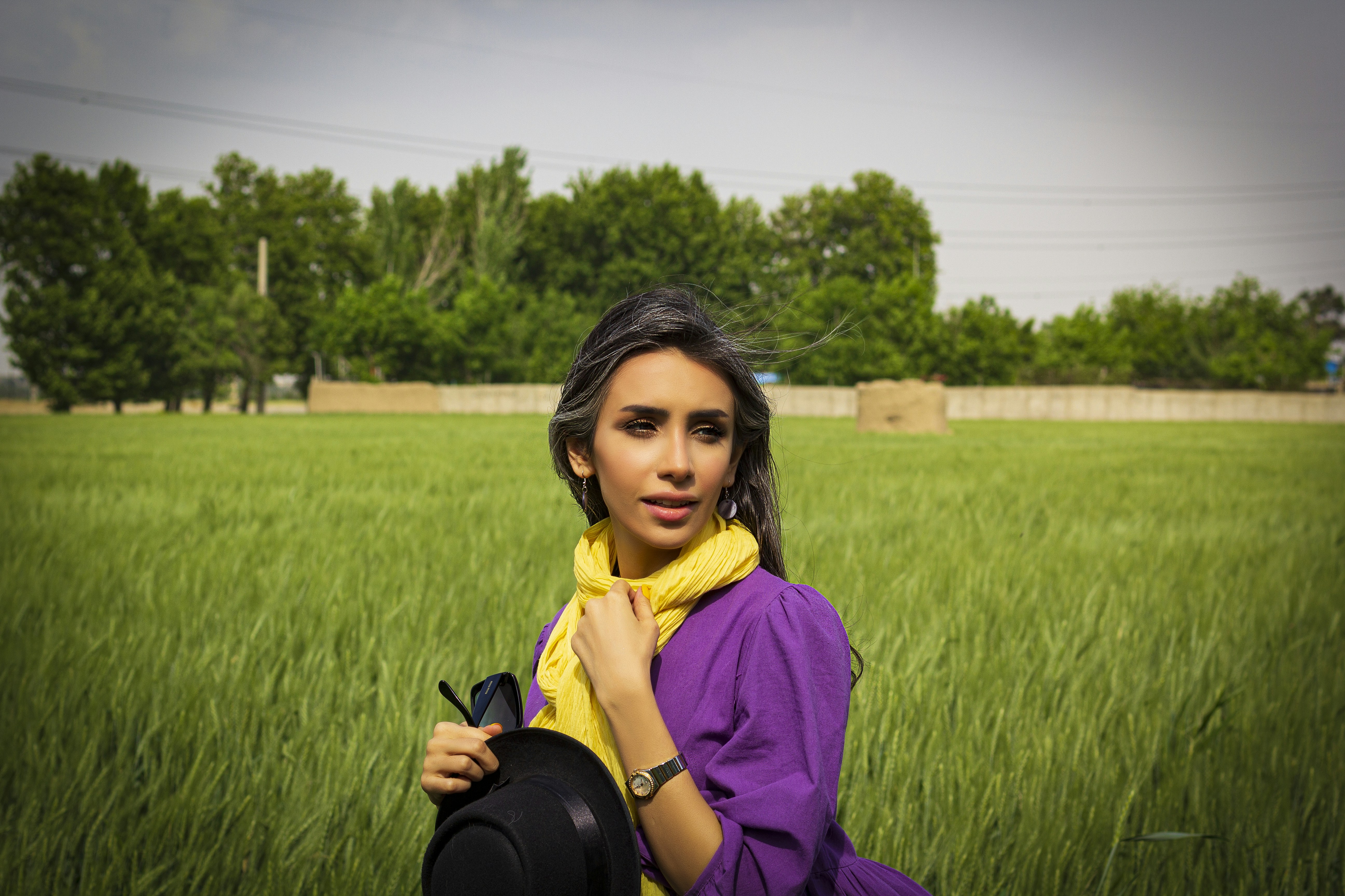 woman in purple long sleeve shirt and black leather sling bag standing on green grass field