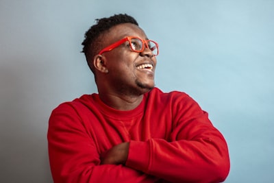 man in red sweater wearing black framed eyeglasses smiling google meet background