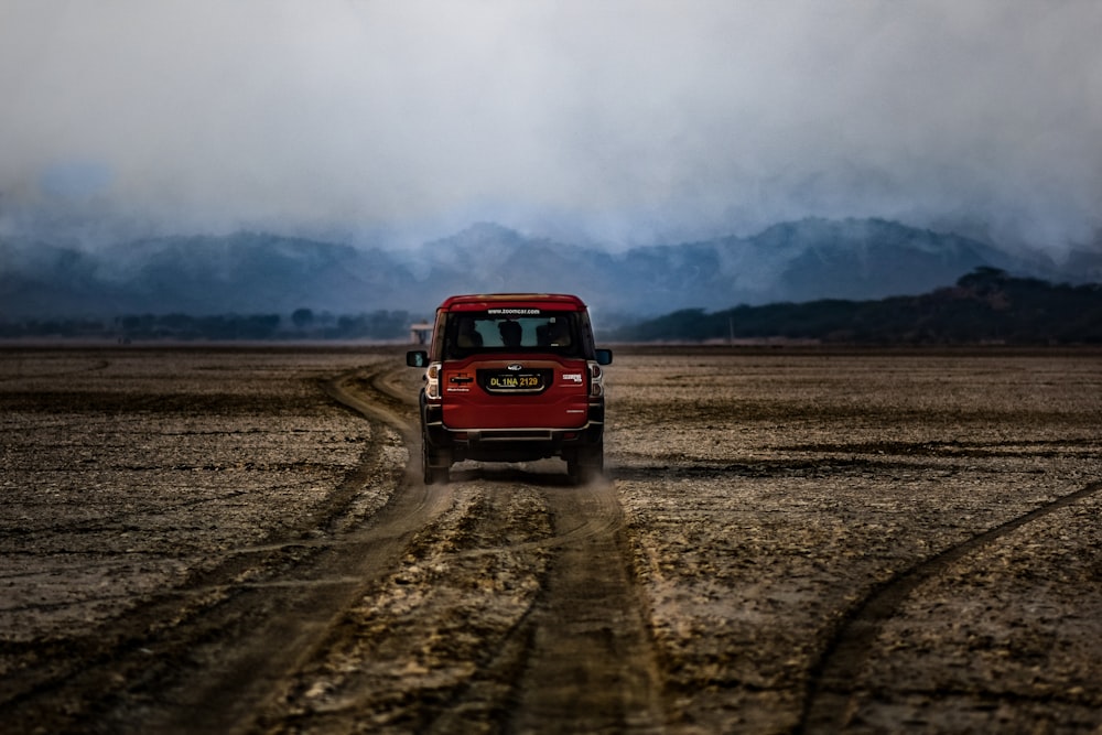 red suv on brown field under white clouds during daytime