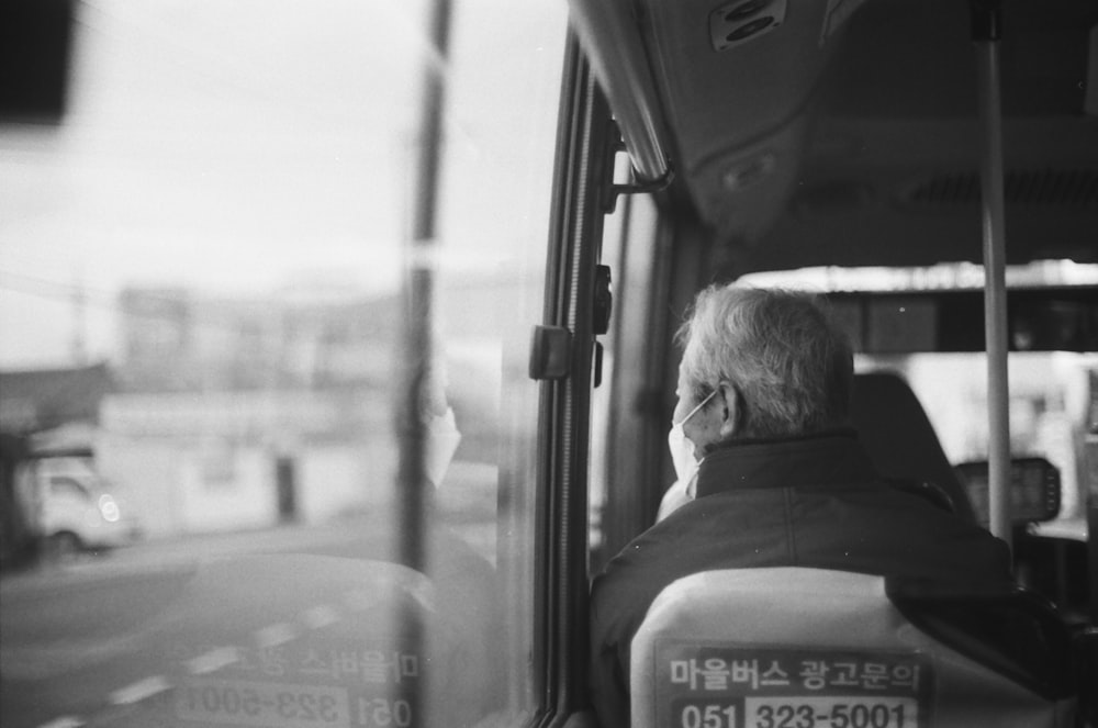 Foto en escala de grises de un hombre con chaqueta sentado dentro de un coche