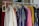 A clothing rack filled with various colorful garments, including dresses and shirts on hangers. A small blackboard sign indicates a sale with prices and discounts.