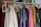 A clothing rack filled with various colorful garments, including dresses and shirts on hangers. A small blackboard sign indicates a sale with prices and discounts.