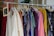 A clothing rack filled with various colorful garments, including dresses and shirts on hangers. A small blackboard sign indicates a sale with prices and discounts.