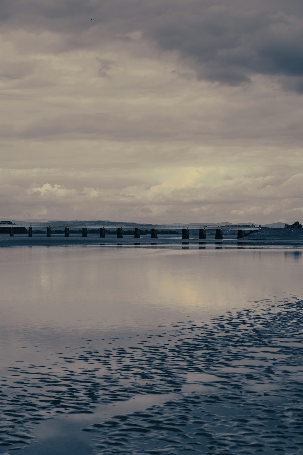 body of water near bridge under cloudy sky during daytime