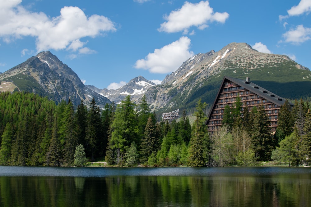 brown wooden house near green trees and lake under blue sky and white clouds during daytime