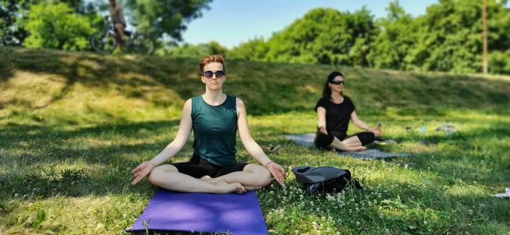 woman in black tank top and blue leggings sitting on purple yoga mat