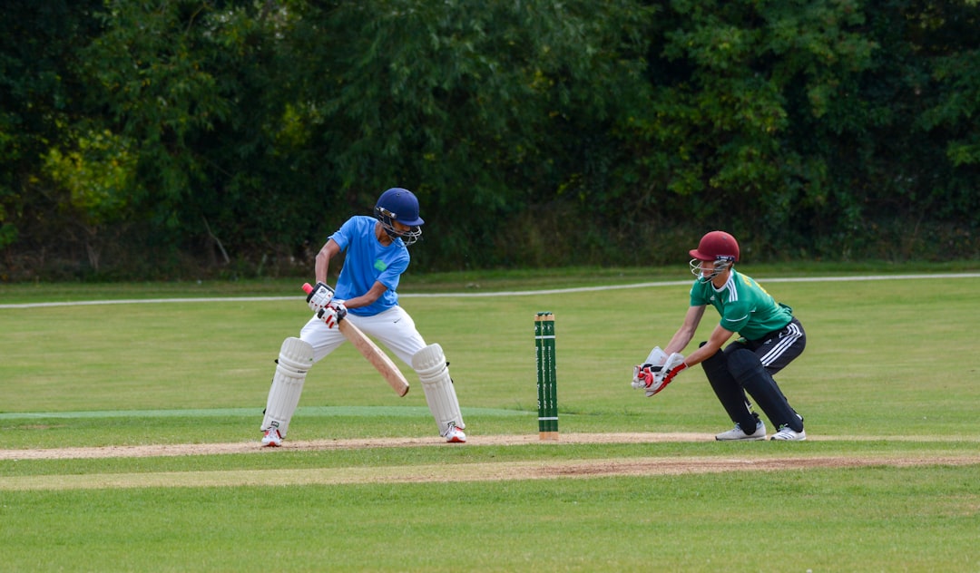2 men playing baseball on green grass field during daytime, Cricket ball in Wicket Keepers gloves