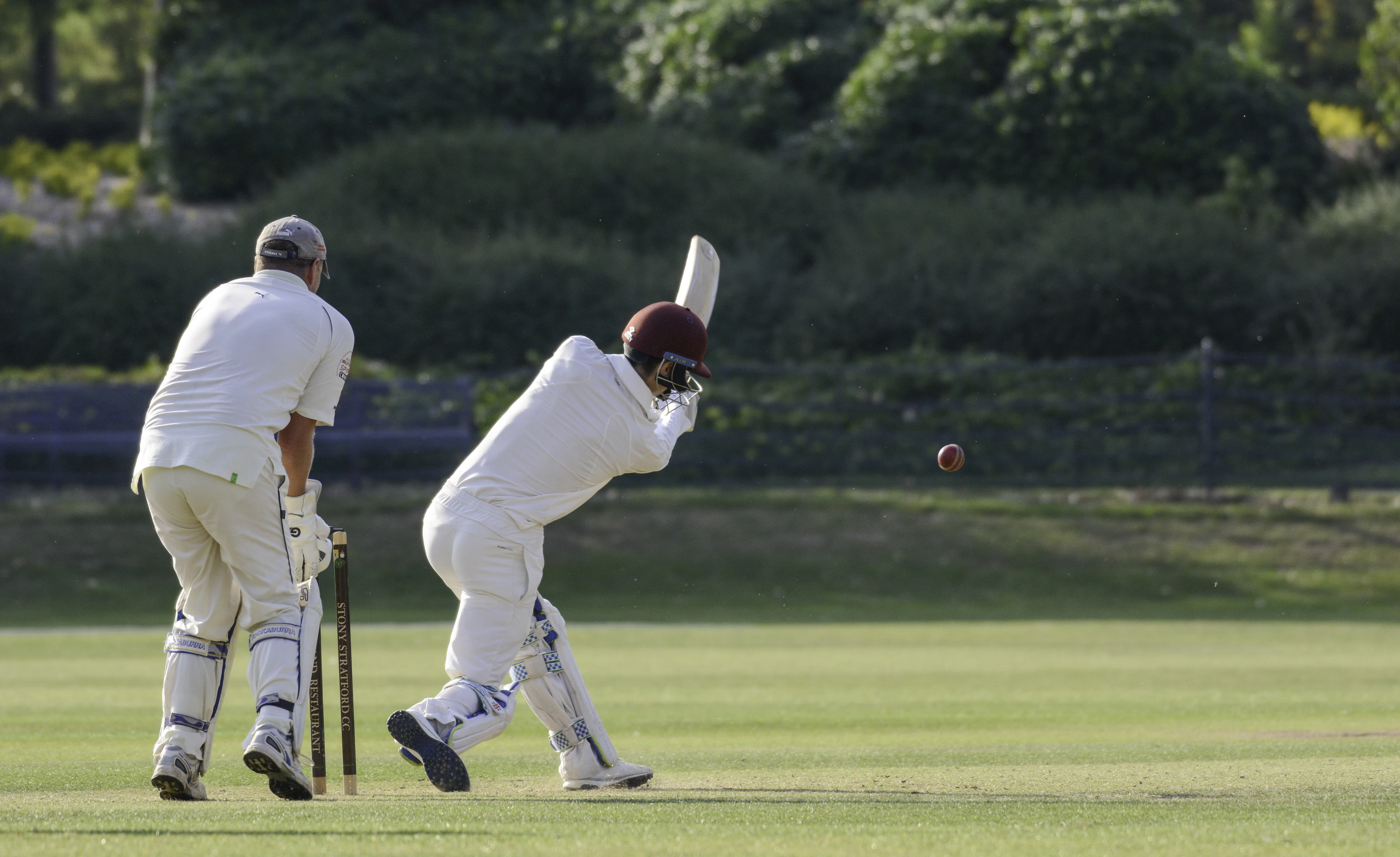 Batter in whites playing a shot as the wicketkeeper crouches behind the stumps