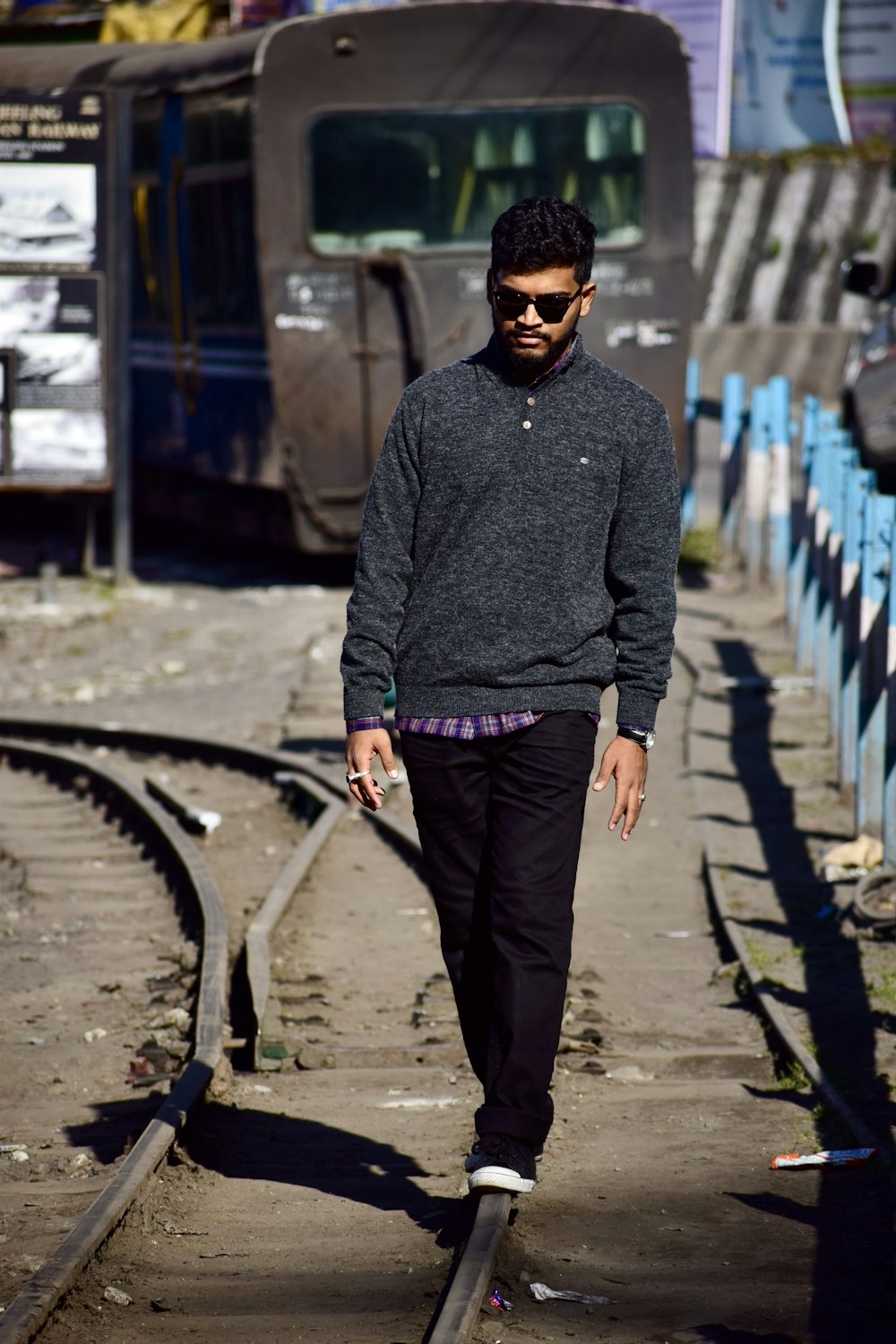 man in gray sweater and black pants standing on train rail during daytime