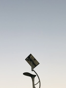 A modern streetlight with a curving pole that includes both a lamp and a solar panel set against a clear sky background. The design is sleek and minimalistic, capturing an innovative and environmentally friendly urban aesthetic.