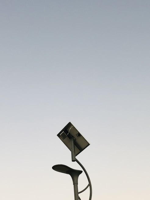 A modern streetlight with a curving pole that includes both a lamp and a solar panel set against a clear sky background. The design is sleek and minimalistic, capturing an innovative and environmentally friendly urban aesthetic.