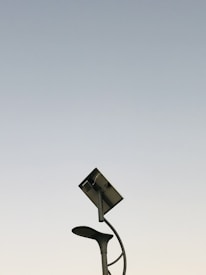 A modern streetlight with a curving pole that includes both a lamp and a solar panel set against a clear sky background. The design is sleek and minimalistic, capturing an innovative and environmentally friendly urban aesthetic.