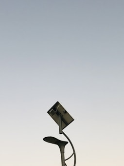 A modern streetlight with a curving pole that includes both a lamp and a solar panel set against a clear sky background. The design is sleek and minimalistic, capturing an innovative and environmentally friendly urban aesthetic.