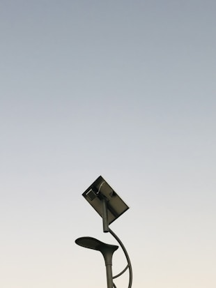 A modern streetlight with a curving pole that includes both a lamp and a solar panel set against a clear sky background. The design is sleek and minimalistic, capturing an innovative and environmentally friendly urban aesthetic.