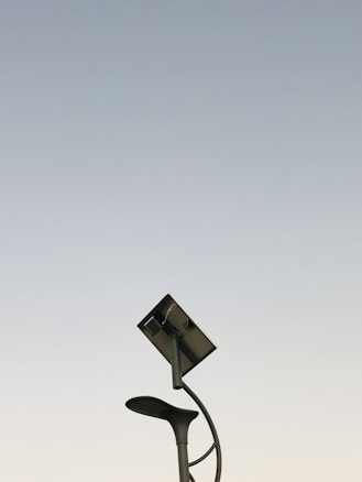 A modern streetlight with a curving pole that includes both a lamp and a solar panel set against a clear sky background. The design is sleek and minimalistic, capturing an innovative and environmentally friendly urban aesthetic.