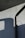 An exterior wall with a textured surface is partially lit by sunlight, casting geometric shadows. A black downspout runs vertically, bending at the top.