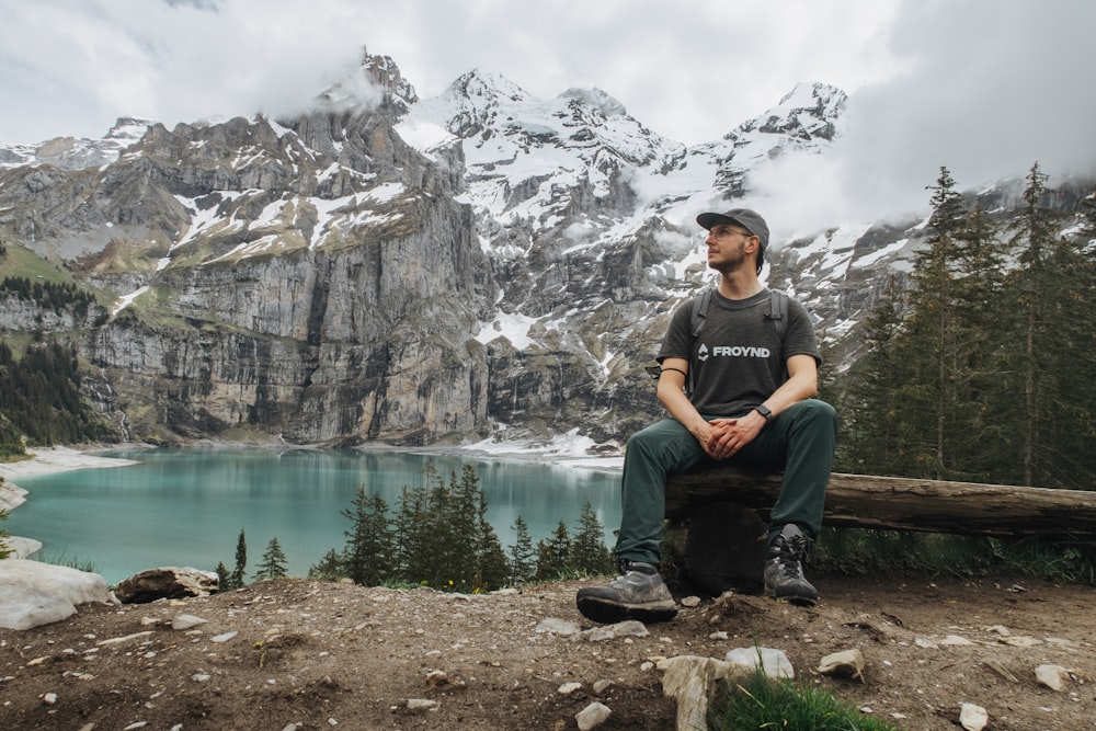 man in black crew neck t-shirt sitting on brown wooden bench near lake during daytime