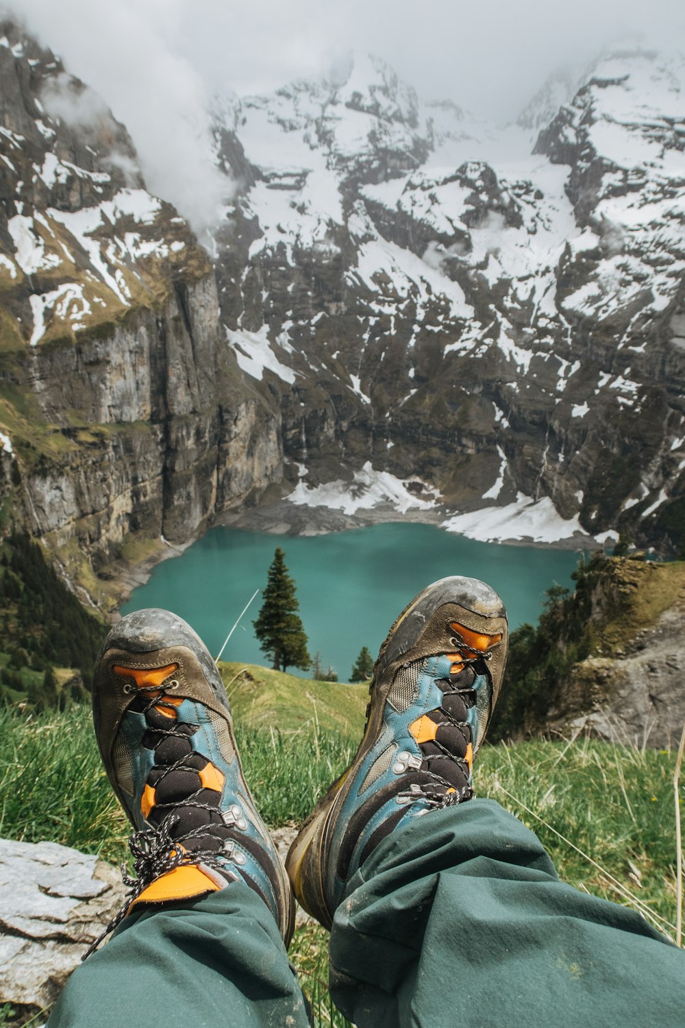 person in black and brown hiking shoes sitting on rock near lake during daytime