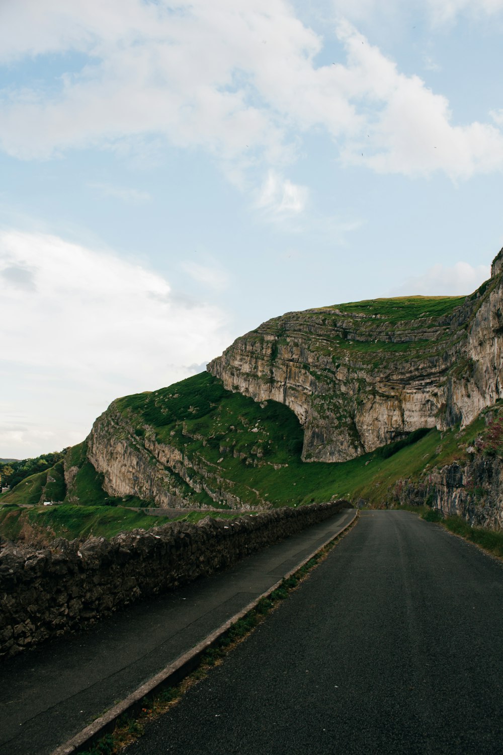 gray asphalt road beside green and brown mountain under white cloudy sky during daytime