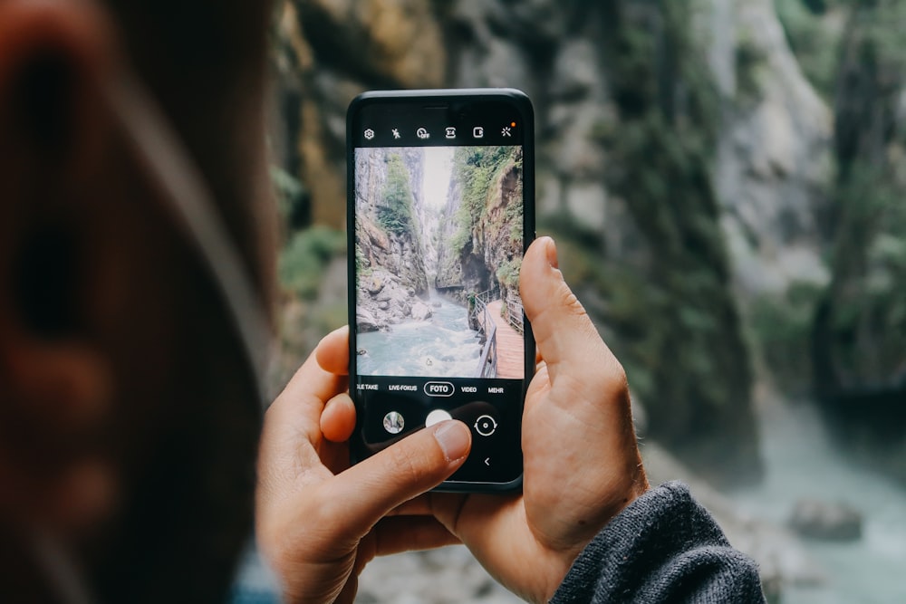 person holding black iphone 4 taking photo of waterfalls