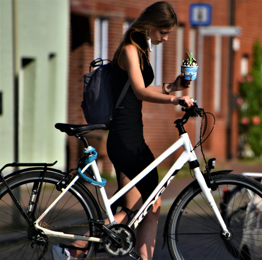 woman in black sleeveless dress standing beside white and blue bicycle during daytime