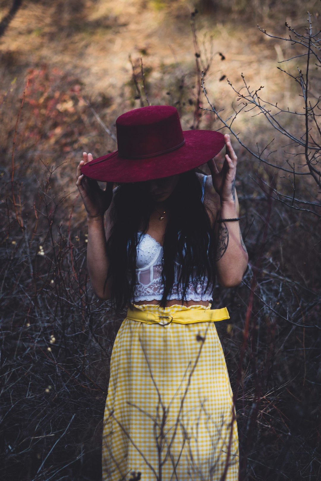 woman in yellow and black plaid dress wearing red hat standing near brown plants
