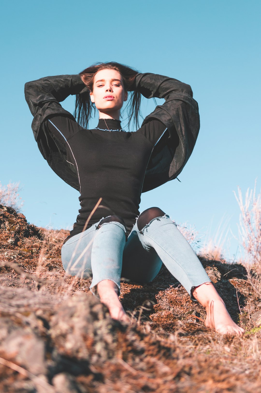 woman in black long sleeve shirt and blue denim jeans sitting on brown grass during daytime
