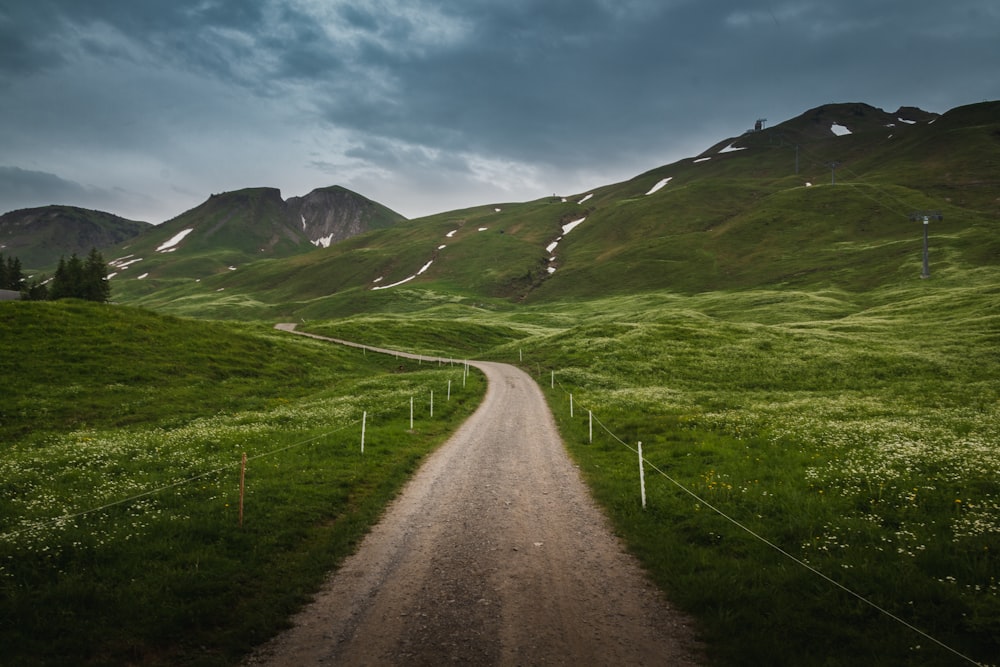 Graue Straße zwischen grünem Grasfeld unter blauem Himmel tagsüber