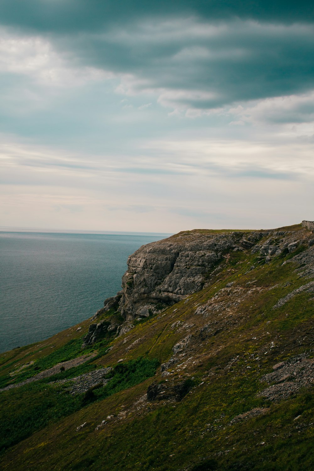 green grass covered mountain beside sea under white clouds during daytime