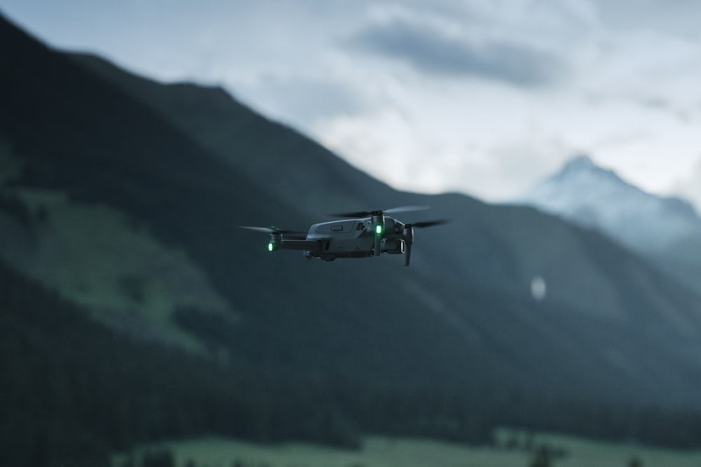 green and white drone flying over green mountain during daytime