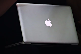 A sleek black MacBook Pro with a glowing blue neon Apple logo on a dark matte surface.