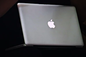 A sleek black MacBook Pro with a glowing blue neon Apple logo on a dark matte surface.
