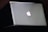 A sleek silver laptop with a prominent glowing Apple logo on its lid, placed on a dark surface.