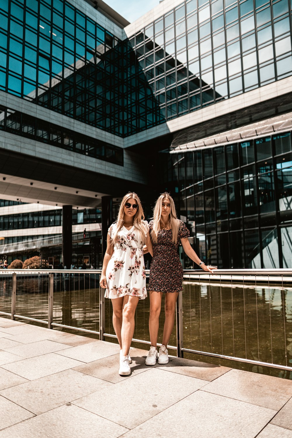 woman in white and black floral dress standing beside glass wall building during daytime