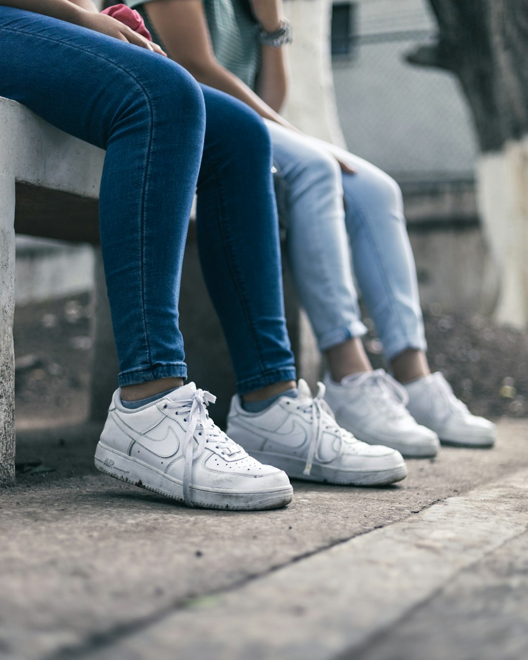 person in blue denim jeans and white nike sneakers sitting on concrete bench