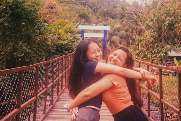 Two people joyfully embracing on a wooden bridge surrounded by lush greenery and palm trees, with a sense of warmth and connection.