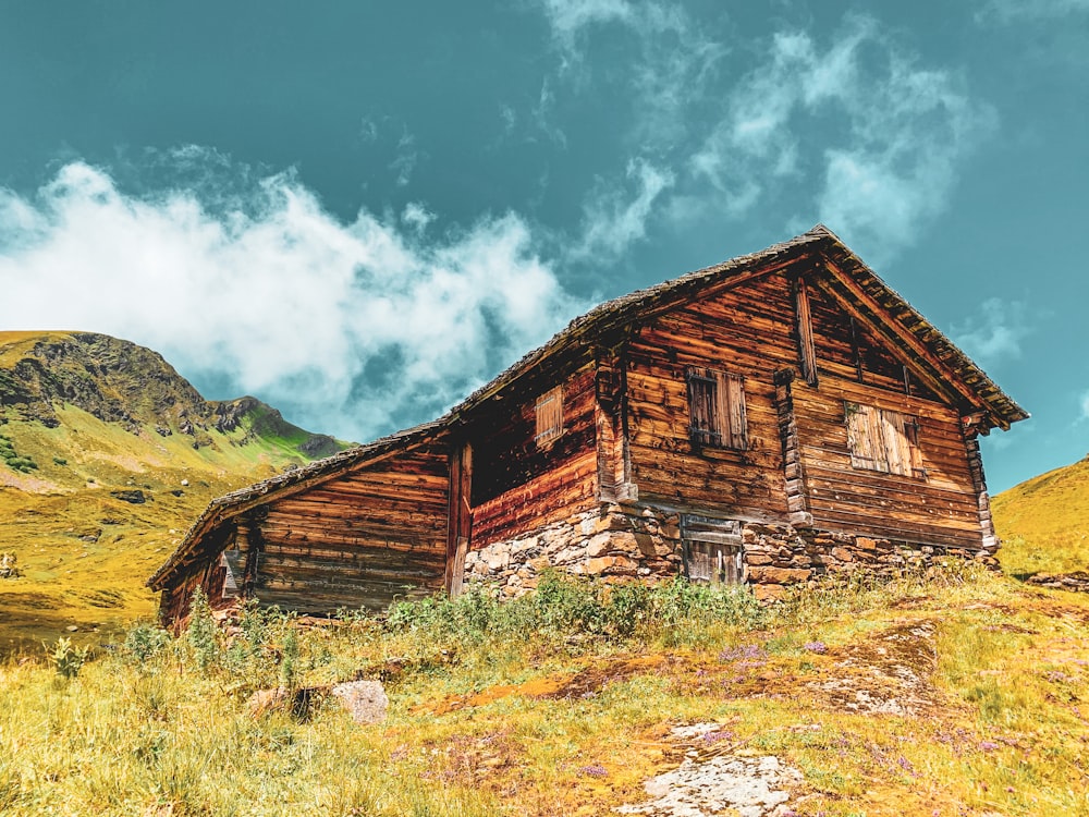 brown wooden house on green grass field near mountain under blue sky during daytime