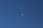 A clear blue sky with a partially visible moon in the center, showcasing its natural beauty and simplicity.