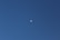 A clear blue sky with a partially visible moon in the center, showcasing its natural beauty and simplicity.