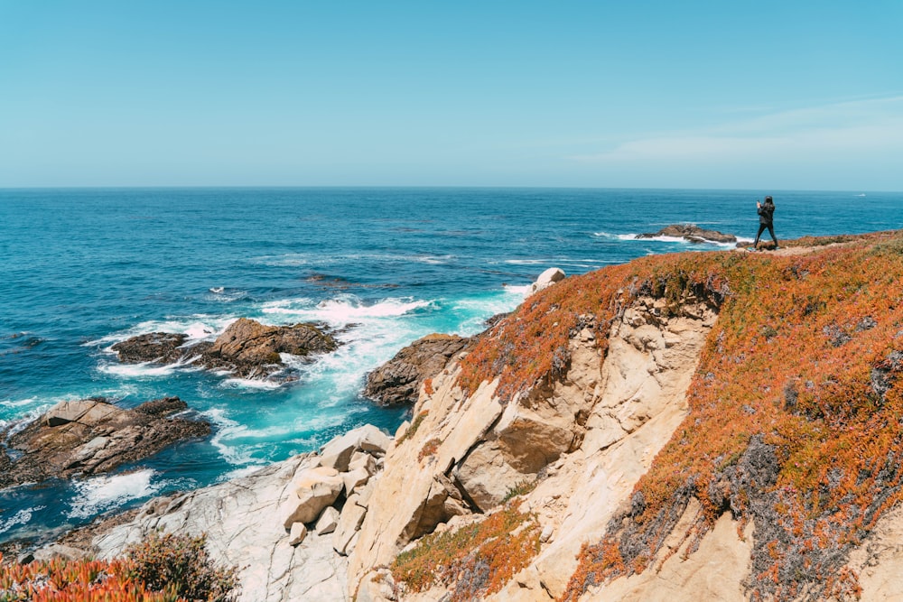 brown and green mountain beside blue sea under blue sky during daytime