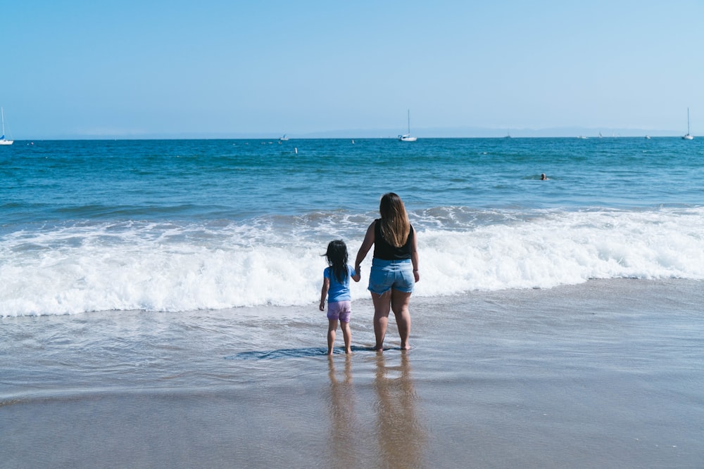 woman in black shirt and blue denim shorts walking on beach during daytime