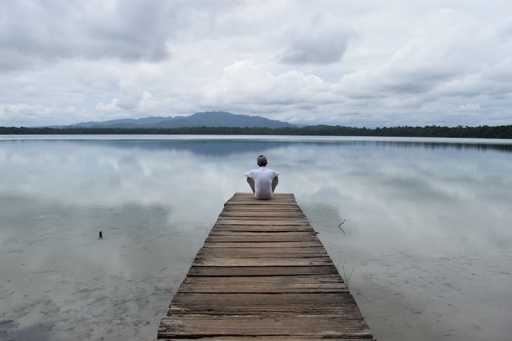 person sitting on wooden dock over the lake during daytime