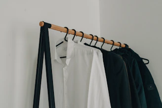 A sleek black blazer hanging on a minimalist gold rack against a white wall.