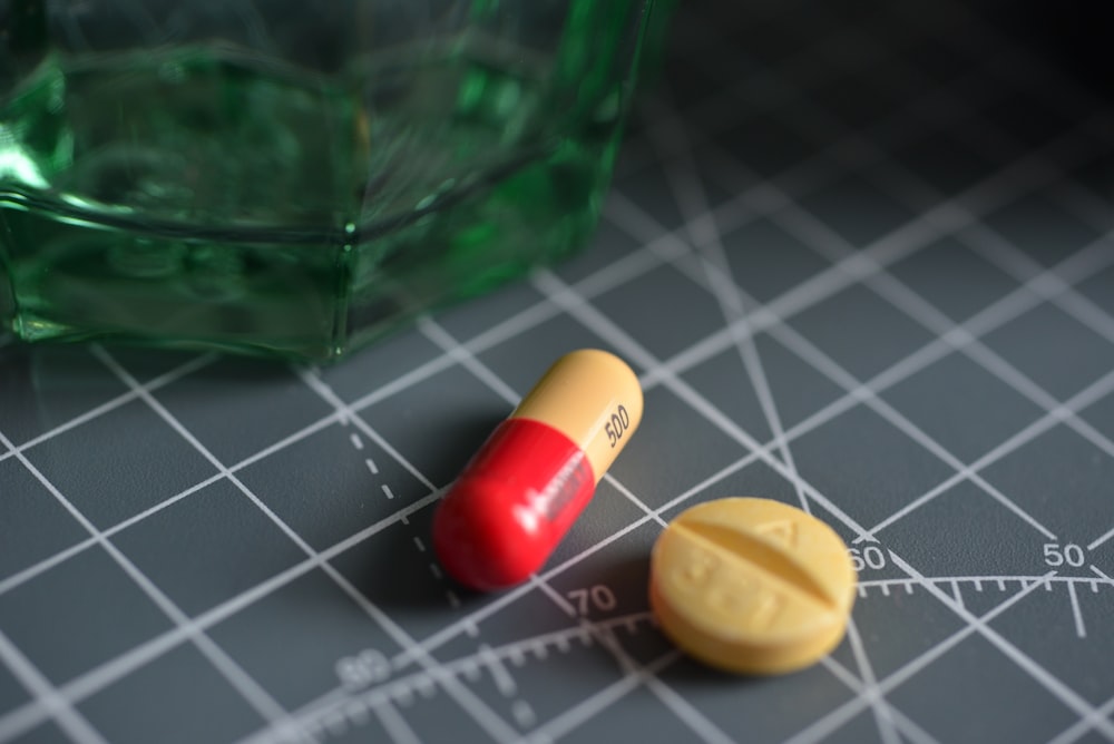 Píldora de medicamento roja y amarilla en frasco de vidrio verde