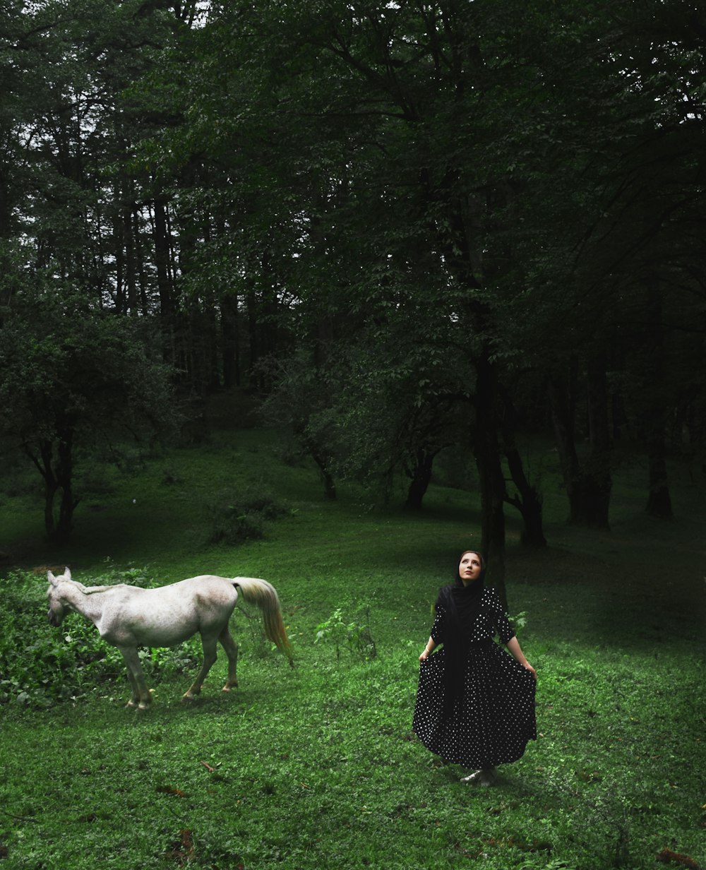 a woman standing next to a white horse on a lush green field