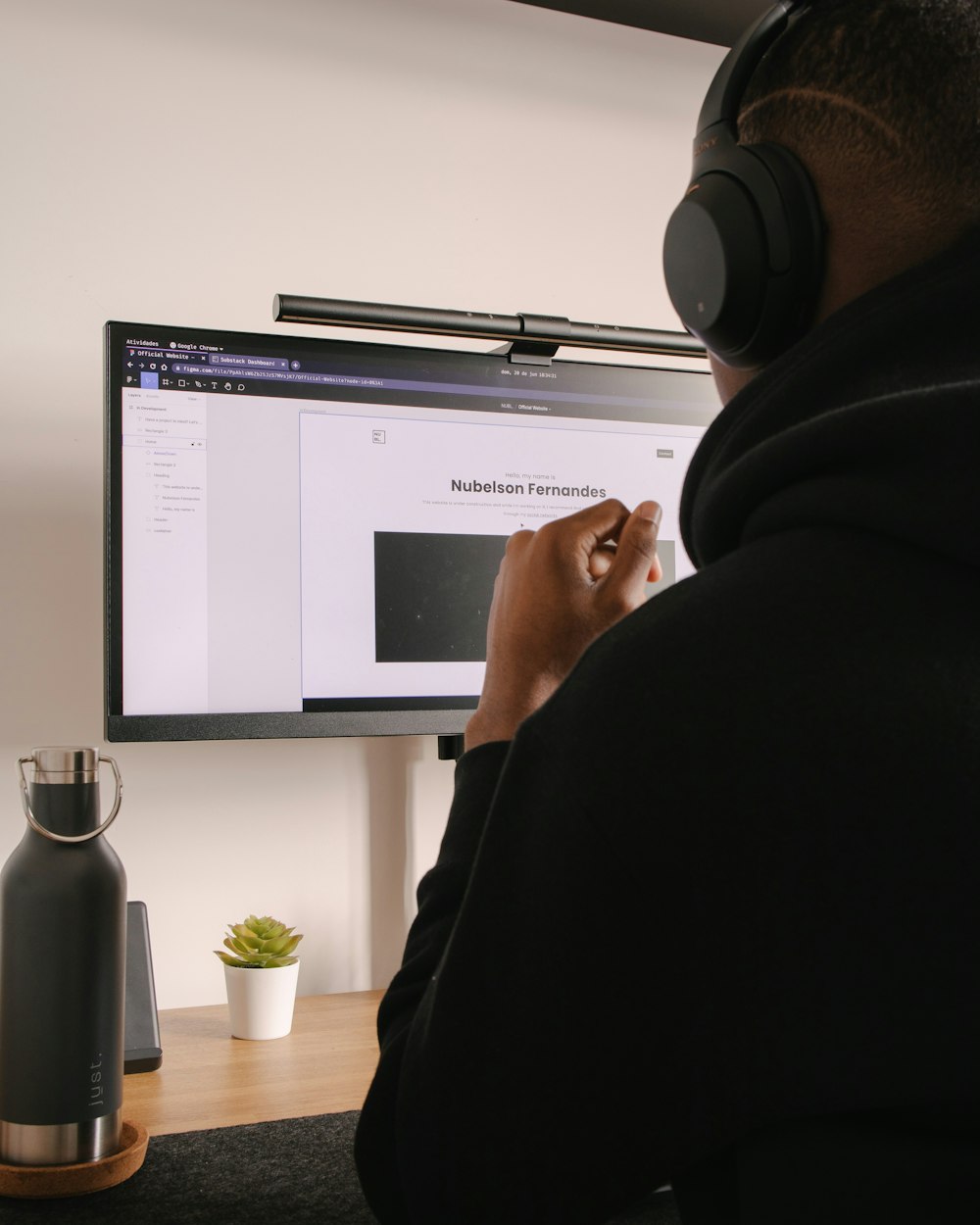 Persona con sudadera con capucha negra sentada frente a un monitor de computadora de pantalla plana negra