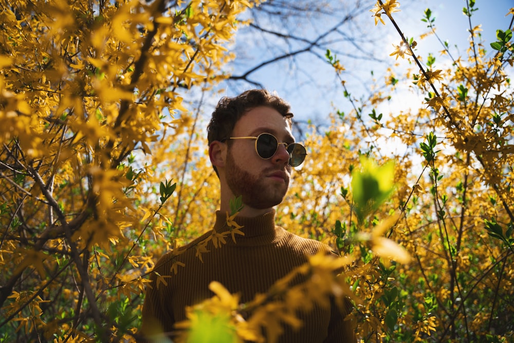 man in brown and black striped crew neck shirt wearing black sunglasses standing under white cherry