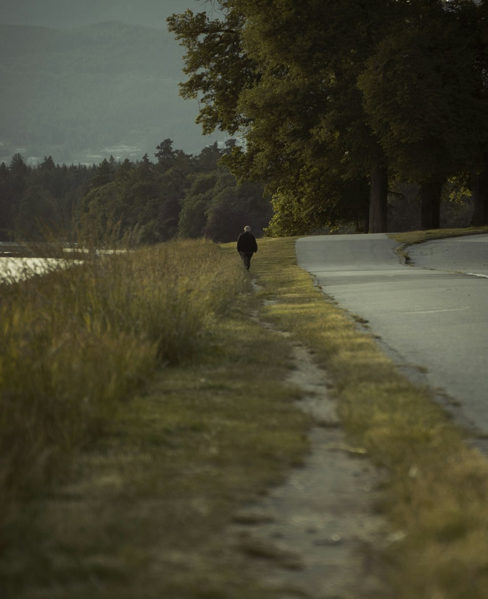 person in black jacket walking on gray concrete road during daytime